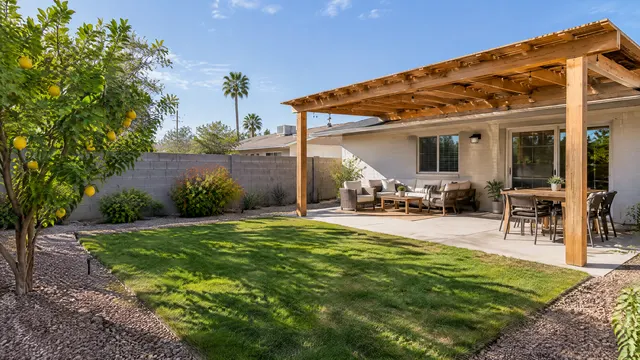 Backyard of a small postwar single-story ranch-style home in the Alhambra area of Phoenix: a new natural wood pergola over a concrete patio, a lemon tree, block wall, gravel and lawn, morning light